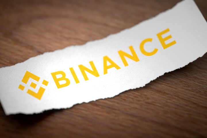 Binance cryptocurrency logo printed on a torn piece of white paper on woodgrain background