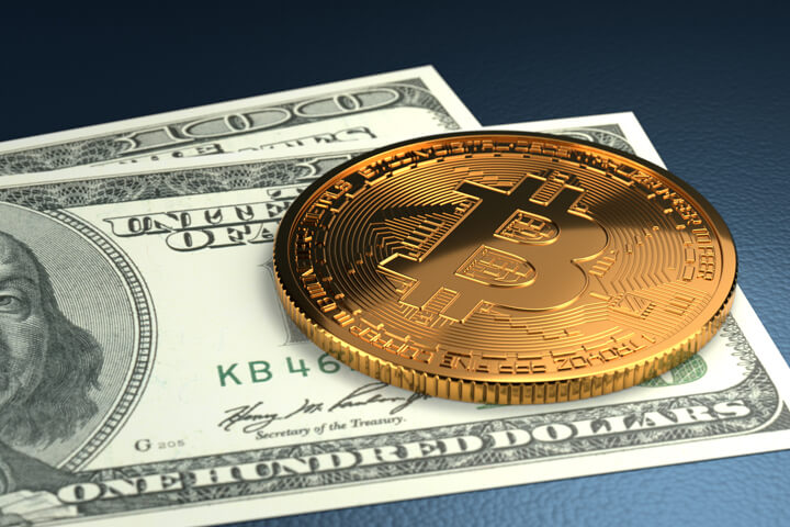 Bitcoin on top of two 100 dollar bills on blue background