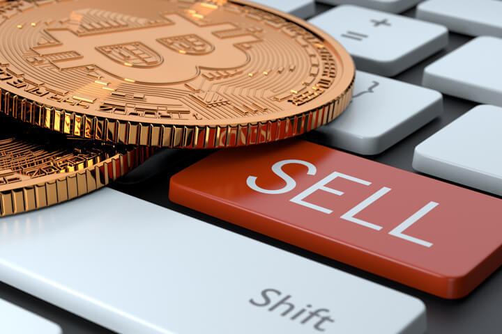 Two Bitcoins laying on keyboard with red Sell key