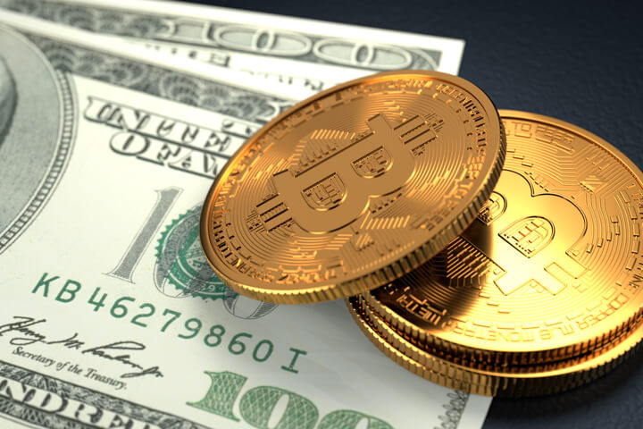 Three Bitcoins laying on top of U.S. one hundred dollar bills