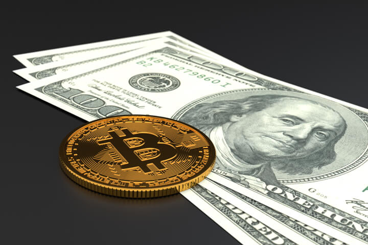 Single Bitcoin laying on top of three U.S. one hundred dollar bills