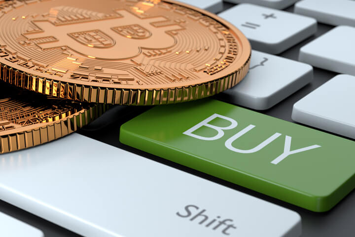 Two Bitcoins on computer keyboard with green Buy key concept for market timing to buy cryptocurrency