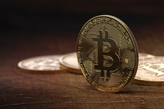 Bitcoin standing on edge Bitcoin balanced on edge in front of blurred row of other Bitcoins in background