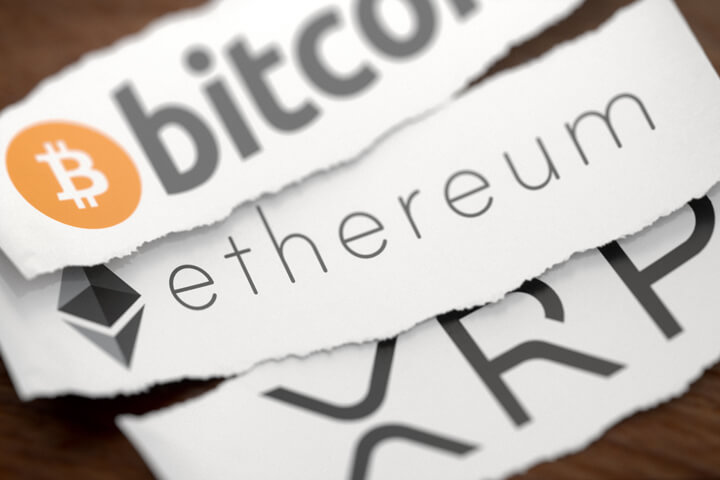 Bitcoin, Ethereum, and XRP cryptocurrency logos printed on torn pieces of paper lying on wood surface