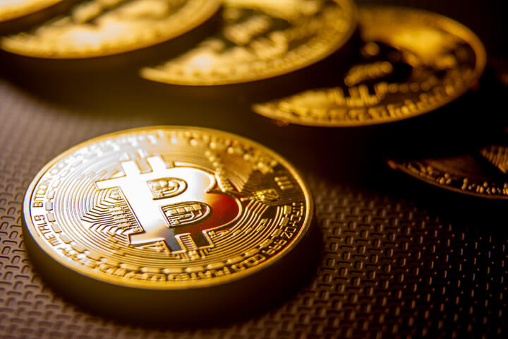 Bitcoin with red reflection in front of blurred line of Bitcoins in background