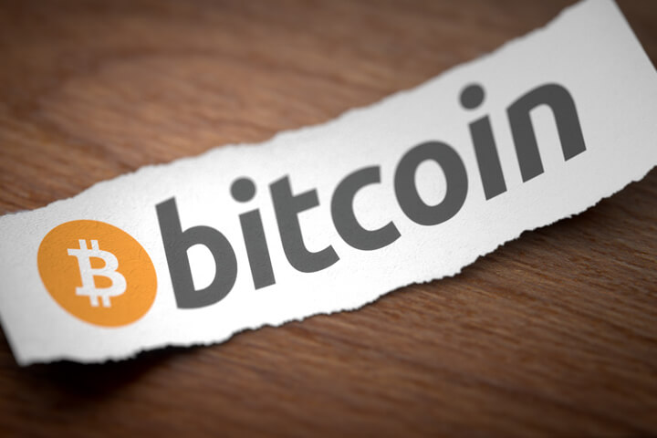 Bitcoin cryptocurrency logo printed on torn piece of scrap paper lying on woodgrain surface