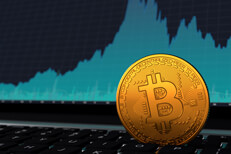 Volatile bitcoin on laptop Bitcoin vertical on laptop keyboard in front of blue price volatility area chart on screen