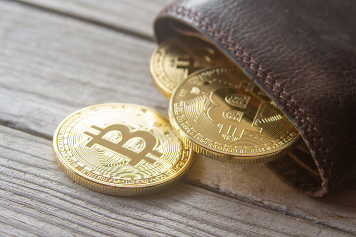 Leather bitcoin wallet with bitcoins protruding and falling out onto wood surface