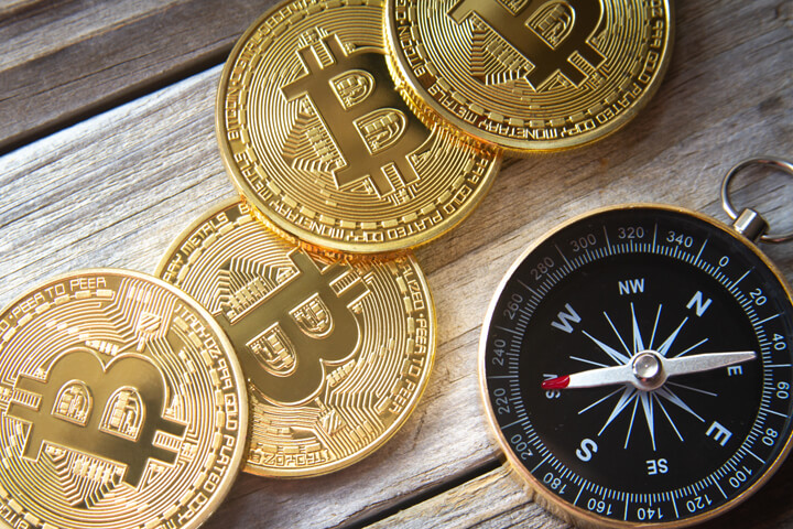 Four Bitcoins next to navigational compass on wood planks
