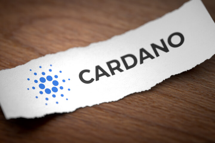 Cardano altcoin cryptocurrency logo printed on torn piece of scrap paper lying on woodgrain surface