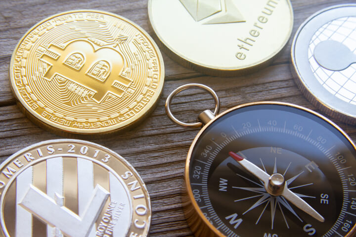 Litecoin, Bitcoin, Ethereum, and Ripple coins with navigation compass pointing at Bitcoin