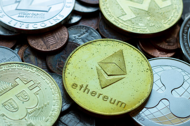 Ethereum, Bitcoin, Litecoin, Monero, and Ripple XRP coins with tarnish lying on assorted U.S. currency coins