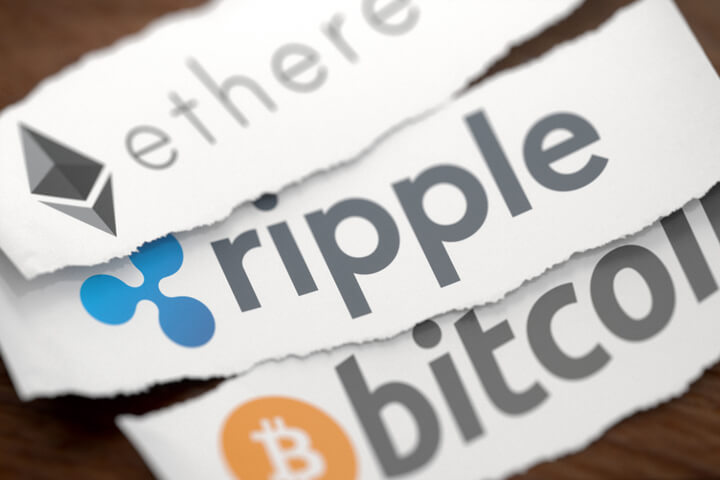 Ethereum, Ripple, and Bitcoin cryptocurrency logos printed on torn piece of white scrap paper lying on woodgrain surface