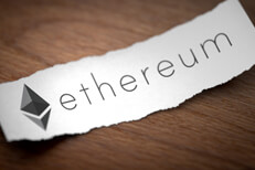 Ethereum logo on torn scrap of paper Ethereum cryptocurrency logo printed on torn piece of black scrap paper lying on woodgrain surface