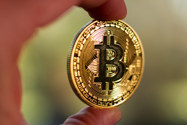 Photo of two fingers holding a Bitcoin with short depth-of-field and background bokeh blur