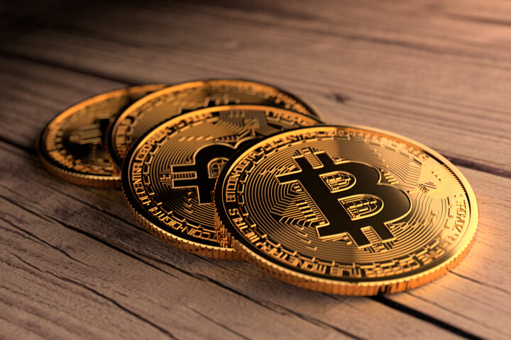 Four Bitcoins laid in a row on weathered wood planks with top right corner lighting