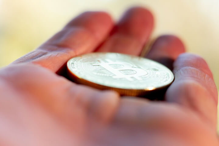 Perspective photo of a hand holding a Bitcoin with short depth-of-field and background bokeh blur