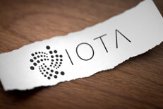 Iota logo on torn piece of paper Iota cryptocurrency logo printed on torn piece of white scrap paper lying on woodgrain surface