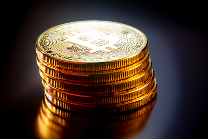 Leaning stack of bitcoins on reflective textured surface with soft back light
