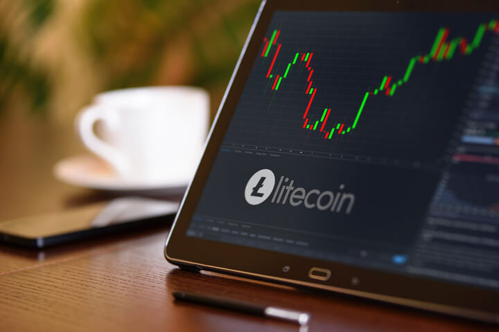 Tablet on desk with coffee cup and cell phone showing Litecoin cryptocurrency logo and stock price candlestick chart