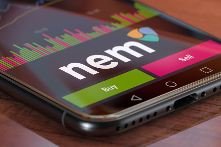 Nem exchange app on iPhone X screen showing Nem logo, trading volume, and option to buy or sell cryptocurrency