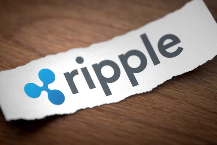 Ripple altcoin cryptocurrency logo printed on torn piece of scrap paper on woodgrain surface