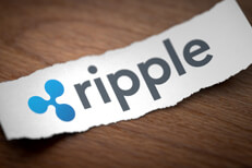Ripple logo on torn scrap of paper Ripple altcoin cryptocurrency logo printed on torn piece of scrap paper on woodgrain surface