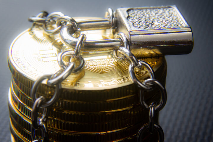 Stack of Bitcoins locked with padlock and chains on dark carbon fiber background