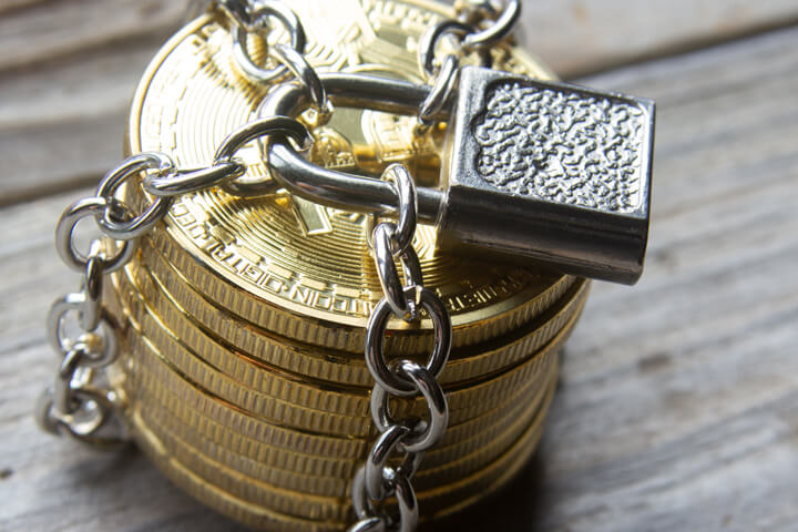 Stack of Bitcoins locked with padlock and chains on weathered wood background