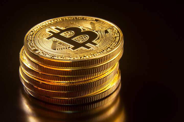 Stack of bitcoins reflected on dark textured surface with black background