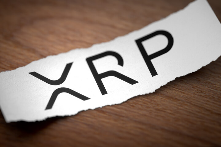 XRP altcoin cryptocurrency logo printed on torn piece of scrap paper on woodgrain surface