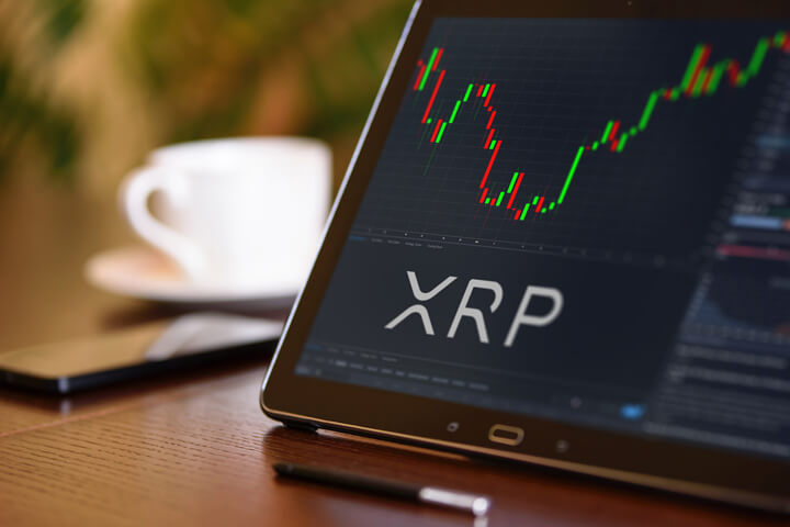 Tablet on desk with coffee cup and cell phone showing XRP cryptocurrency logo and stock price candlestick chart