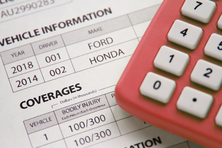 Calculator sitting on car insurance policy showing vehicle information and policy coverages