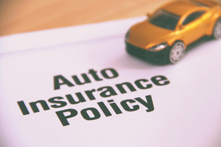 Small yellow car placed on top of an auto insurance policy on a desk