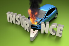 Car insurance concept photo of blue car on fire crashed into stone letters spelling INSURANCE