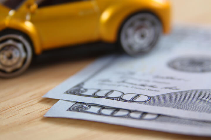 Toy car on wood desk with two one hundred dollar bills
