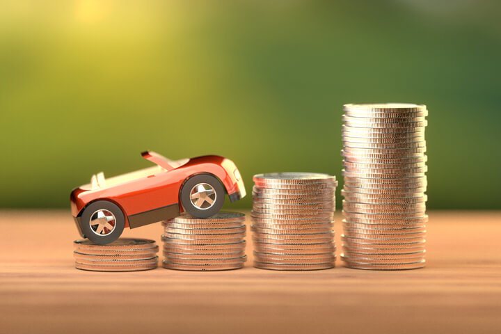 Toy car climbing increasing stacks of coins symbolizing increasing cost of car insurance