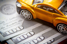 Toy car on top of fanned 100 dollar bills car insurance cost concept photo