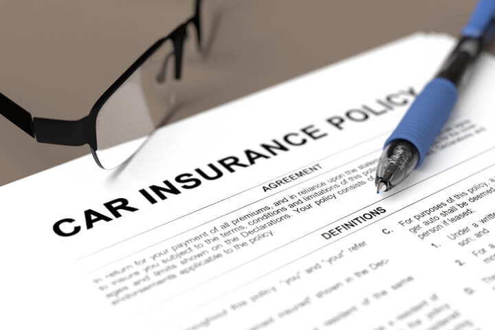 Car insurance policy on desk with pen and glasses