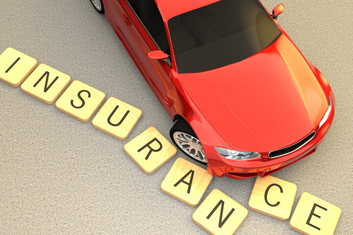 Red car sliding and displacing several wooden letters spelling insurance