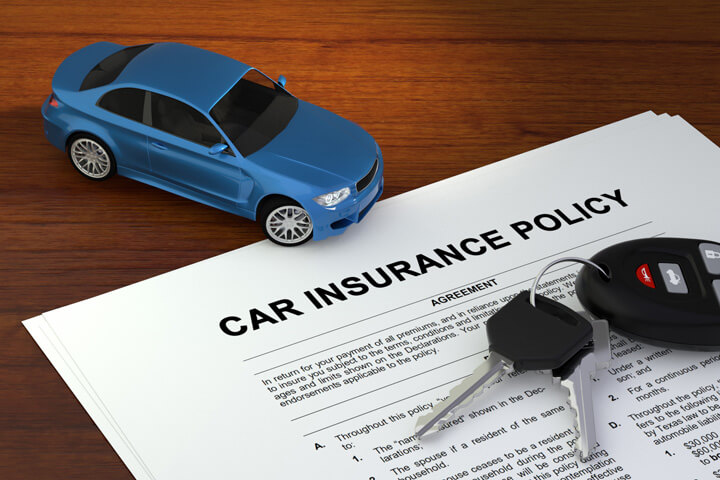 Car insurance policy on wood desk with small blue car and car keys