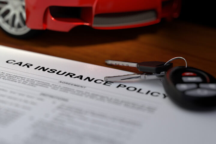 Close up of car insurance policy with car keys and sports car in background