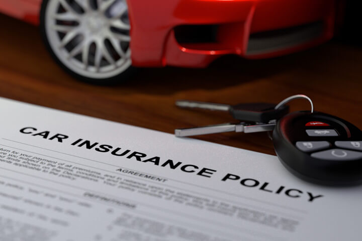 Car insurance policy on wood desk with model car and car keys with key fob