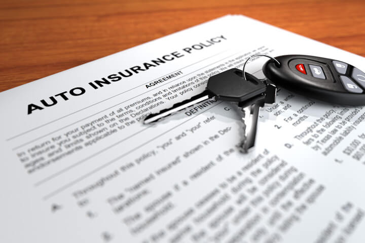 Auto insurance policy on desk with car keys and door clicker