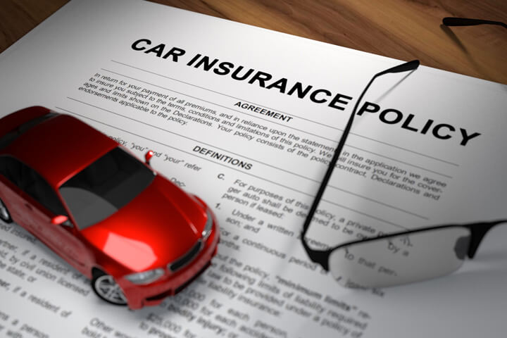 Car insurance policy with reading glasses on desk with red toy car