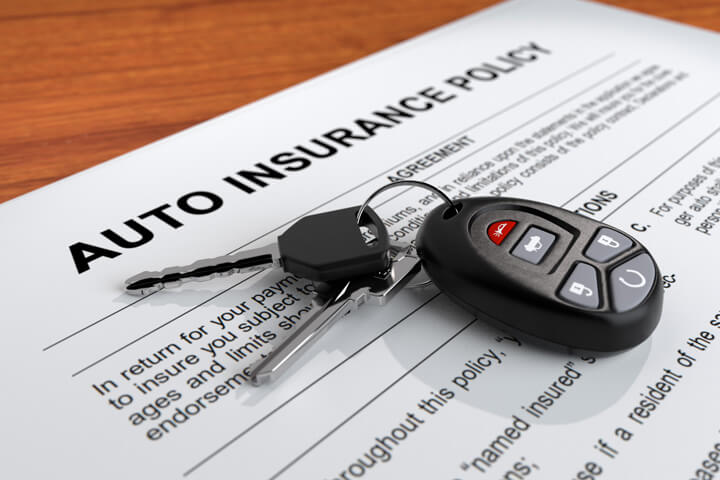 Auto insurance policy on desk with car keys and door clicker