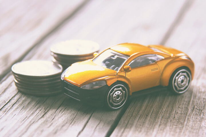 Stacks of coins with small toy car on weathered wood planks