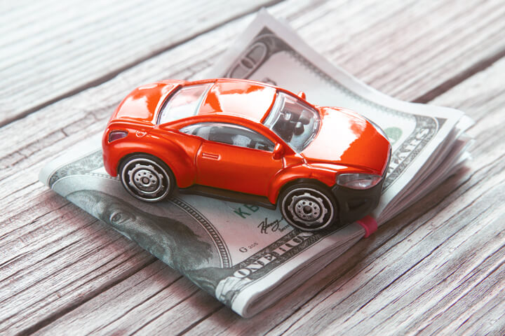 Red toy car on top of folded 100 dollar bills car insurance or automotive costs concept photo