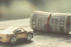 Vintage version of small car next to roll of money Vintage photo of small toy car next to roll of money wrapped in rubber bands