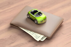 Green toy car on top of wallet Green toy car sitting on top of wallet with corners of bills sticking out from wallet on wood table